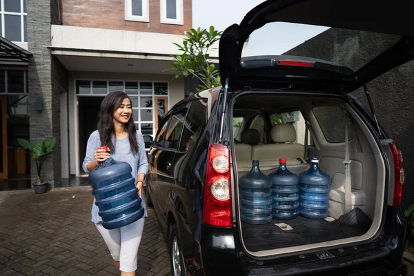 Mulher carregando um galão de água colocar no porta-malas do carro — Fotografia de Stock