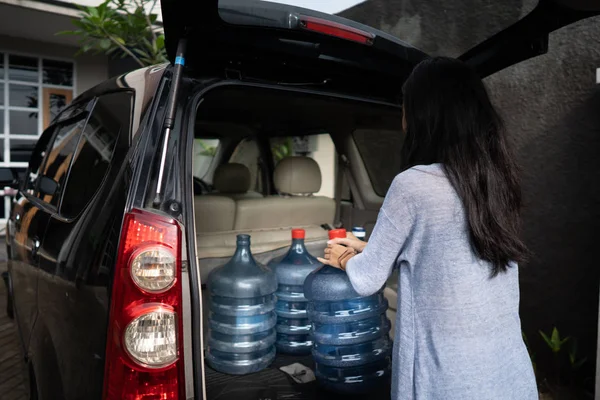 Mulher carregando um galão de água colocar no porta-malas do carro — Fotografia de Stock