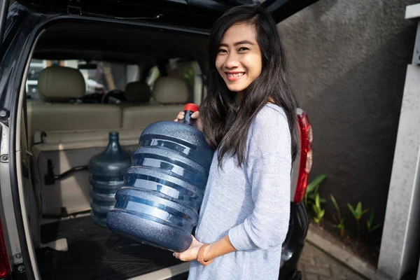 Mulher carregando um galão de água colocar no porta-malas do carro — Fotografia de Stock