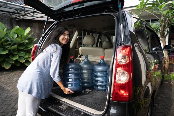 woman carrying a gallon of water put in car trunk