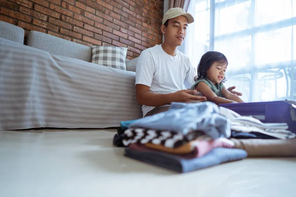 Asiatischer junger Mann mit einer Tochter sitzt und legt seine Kleidung in einen Koffer — Stockfoto