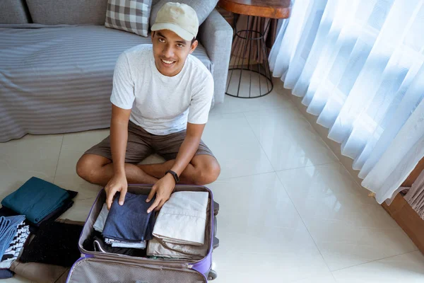 Aziatische jonge man kijken naar de camera bij de voorbereiding van zijn kleren voordat u gaat reizen — Stockfoto