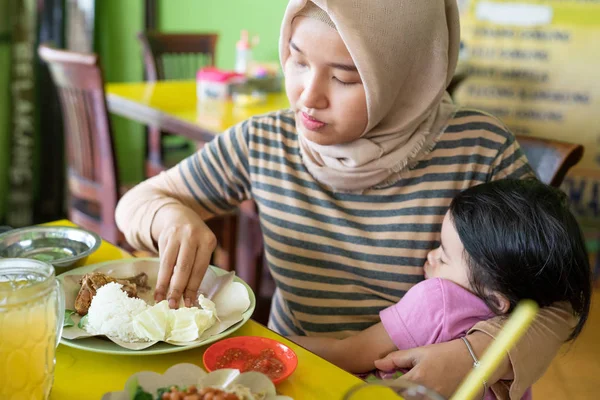 Retrato de uma mãe hijab carregando sua filha enquanto come — Fotografia de Stock