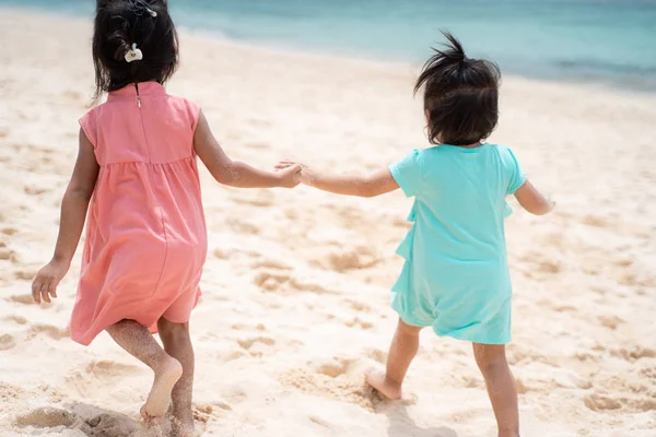 Two little girl walking together on white sand beach from behind view — Stock Photo, Image