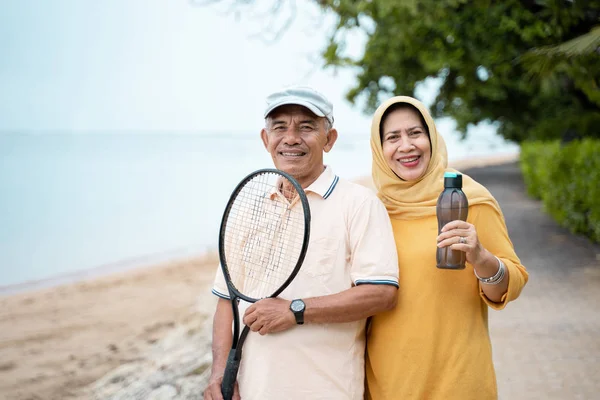 portrait of senior asian man and woman smiling with racket tennis in hand