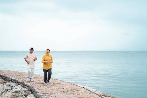 Seniorin und Mann laufen gemeinsam am Strand — Stockfoto