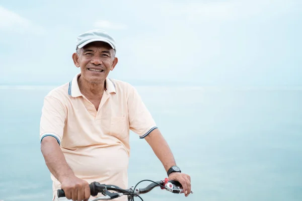 Aziatische oude man paardrijden zijn fiets op het strand — Stockfoto