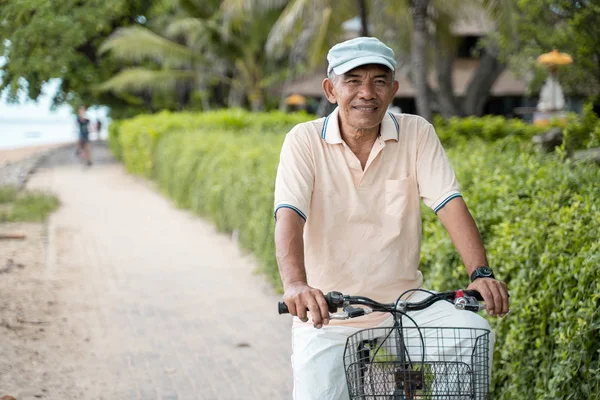 Asiatico vecchio equitazione la sua bicicletta a il spiaggia — Foto Stock