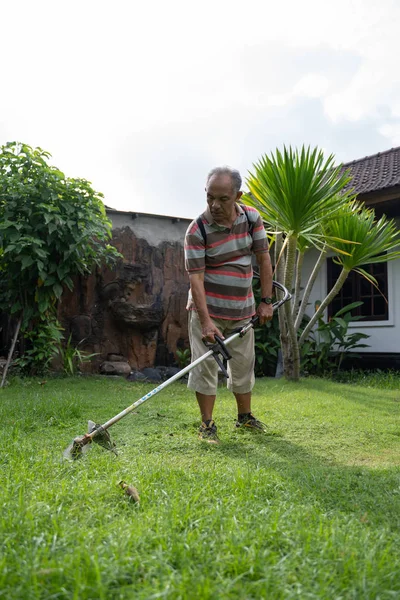 Viejo asiático hombre segando su jardín — Foto de Stock