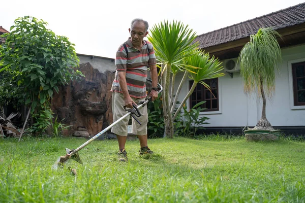 Старий азіатський чоловік косить свій сад — стокове фото