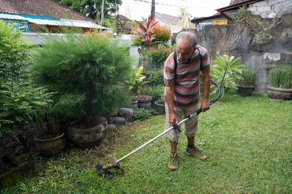 Senior asiático hombre siega hierba en su propio hogar jardín — Foto de Stock