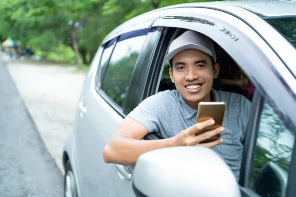 Молодой человек-водитель использует смартфон, чтобы посмотреть на камеру — стоковое фото