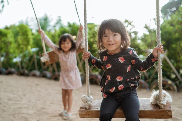 Retrato de una niña feliz riendo cuando juega un swing con amigos —  Fotos de Stock