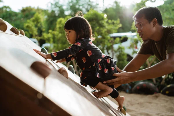 Porträt eines kleinen Mädchens beim Versuch, mit Hilfe ihres Vaters von hinten zu klettern — Stockfoto
