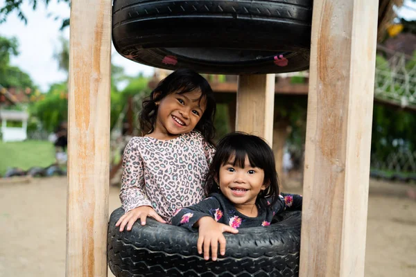 Deux filles heureuses regardent la caméra en jouant ensemble sur le trou des pneus — Photo