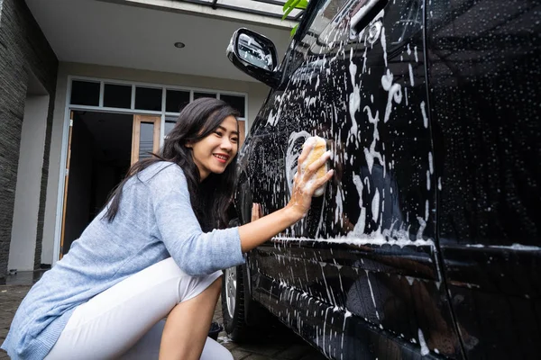 Mulher limpeza e lavagem de seu carro preto — Fotografia de Stock