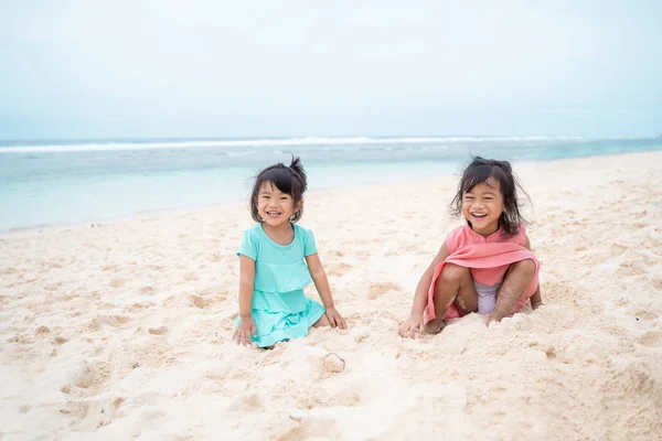 Two daughter sit down on white sand smiling — Stock Photo, Image