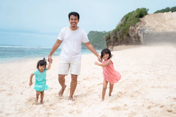 Otec drží ruce dvě dcery na pláži — Stock fotografie