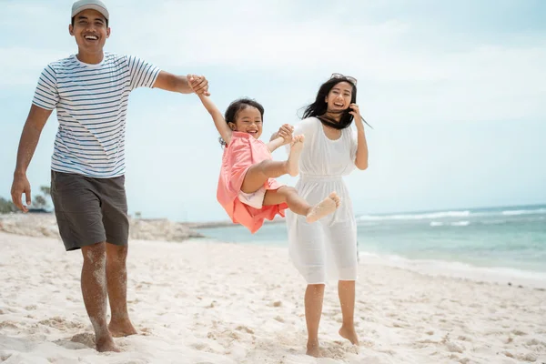 Pai e mãe balançando uma menina na praia — Fotografia de Stock