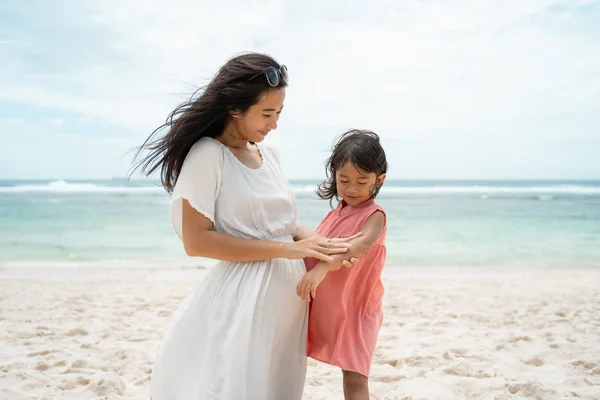 Filha olhar seu braço quando uma mãe esfregar protetor solar — Fotografia de Stock