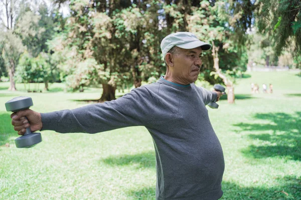 Ανώτερος αρσενικό κάνει άσκηση στο πάρκο και κρατώντας αλτήρα — Φωτογραφία Αρχείου