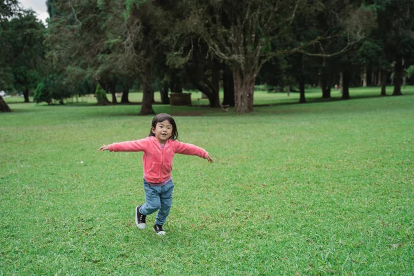 Småbarn som kör i parken och spridning öppna hennes hand — Stockfoto