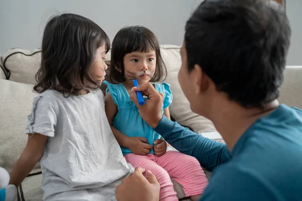 爸爸有乐趣与他的孩子通过使一些在女儿的脸上的脸画 — 图库照片