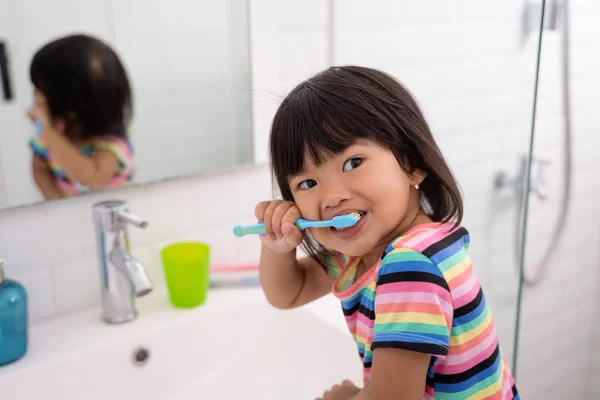 Asiatiska liten flicka borstar hennes tänder och hennes huvud ser när kallas av sin mor — Stockfoto