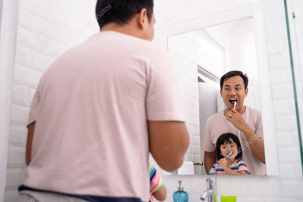 girl brushing teeth in bathroom sink with dad