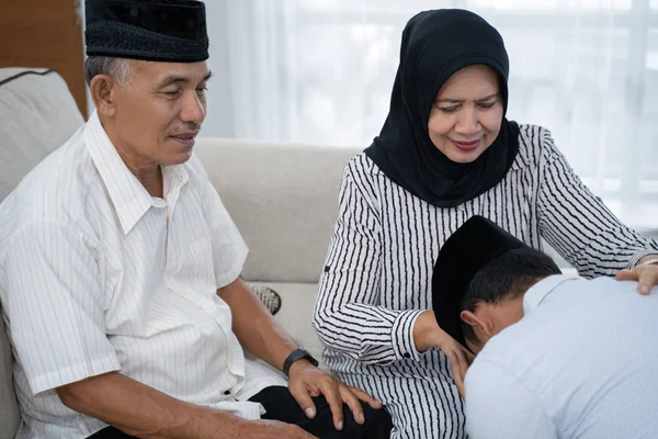 Hombre arrodillado y besar a sus padres mano pidiendo perdón — Foto de Stock