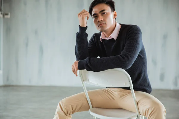 Pose de cerca de un hombre de negocios casual sentado en una silla blanca en el pasillo — Foto de Stock