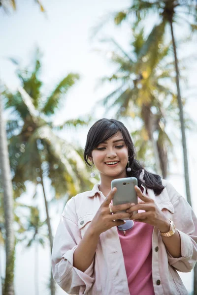 Vrouw texting met smartphone onder de kokosnoot bomen — Stockfoto