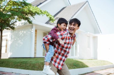 father piggyback ride with his son in front of the house clipart