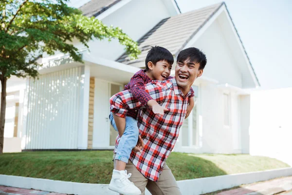 father piggyback ride with his son in front of the house