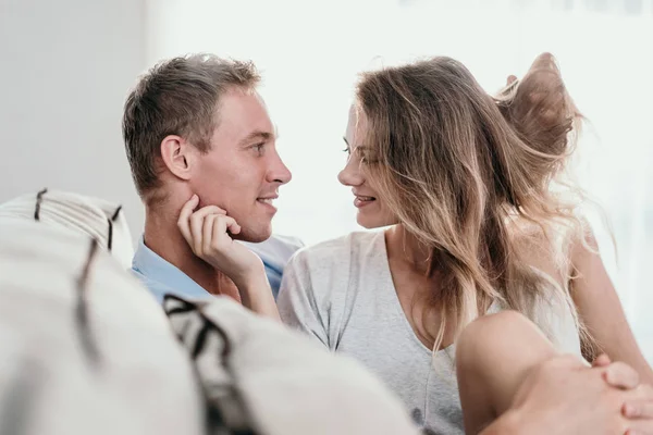 Jovem casal abraçando enquanto sentado cara a cara em um sofá — Fotografia de Stock