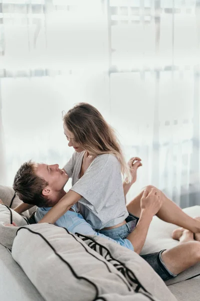 Joven pareja abrazando mientras se sienta cara a cara en un sofá —  Fotos de Stock