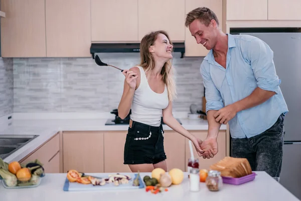 Νεαρό ζευγάρι να κρατήσει τα χέρια και να αρχίσετε να χορεύετε όταν προετοιμαστείτε για το μαγείρεμα — Φωτογραφία Αρχείου