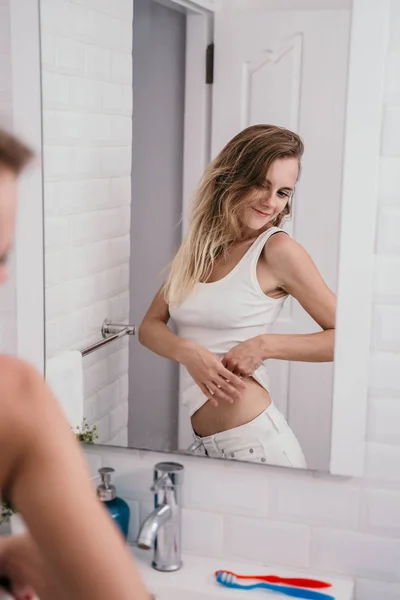 Женщина смотрит на себя перед зеркалом и показывает желудок — стоковое фото