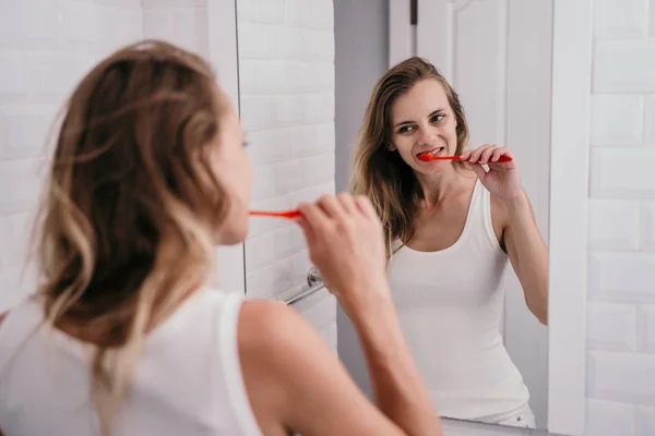 Ung kvinna borsta tänderna framför spegeln — Stockfoto