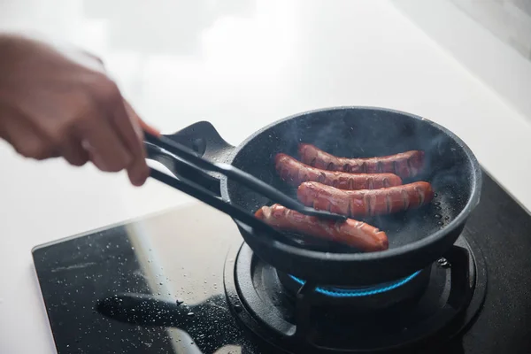 Hands using food tongs to frying sausages — Stock Photo, Image