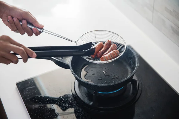 소시지 튀김에 음식 집게를 사용하여 손을 — 스톡 사진