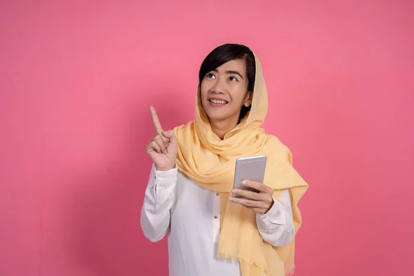 Wanita muslim menunjuk ke atas sambil memegang telepon — Stok Foto