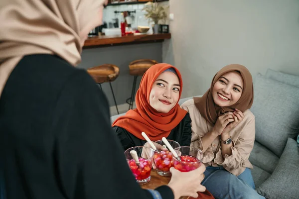 Wanita muda terselubung menyajikan koktail buah-buahan untuk teman-temannya ketika mengobrol bersama di rumah — Stok Foto