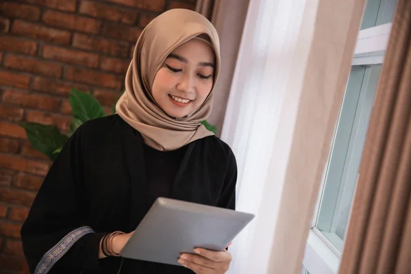Junge Frau trägt Hidschab und sieht ein Tablet, das in der Nähe von Fenstern steht — Stockfoto
