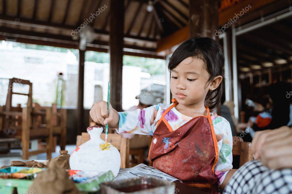 child painting ceramic pot with paint brush