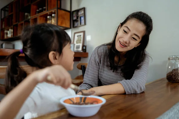 Маленькая азиатская девочка ест хлопья на завтрак с мамой — стоковое фото