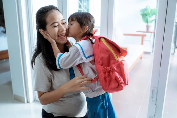 Mała dziewczynka ze szkołą mundur całować jej mama w domu — Zdjęcie stockowe