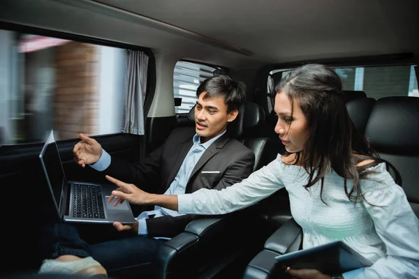 Businessman and woman using laptop on passenger seat of car — Stock Photo, Image