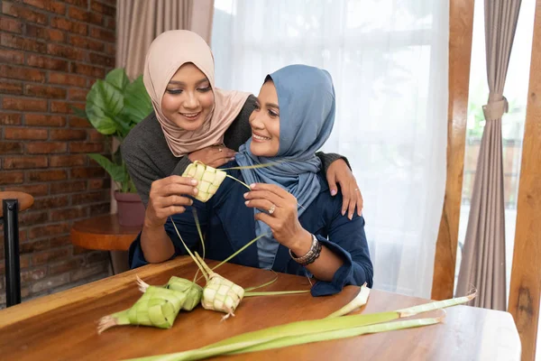 Två beslöjade kvinna gör en vävd omslag av ketupat — Stockfoto