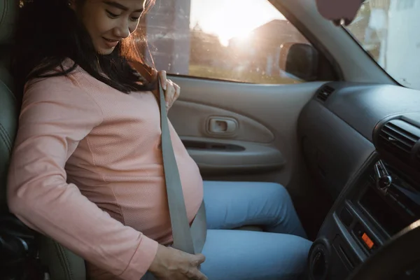 Беременная женщина пристегивает ремень безопасности, сидя на машине — стоковое фото